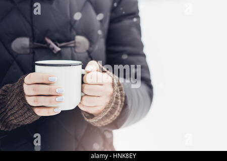 Frau mit weißem rustikalen Becher Glühwein mit Gewürzen und Zitrusfrüchten in ihre Hände im Freien in kalten Wintertag, Nahaufnahme Stockfoto
