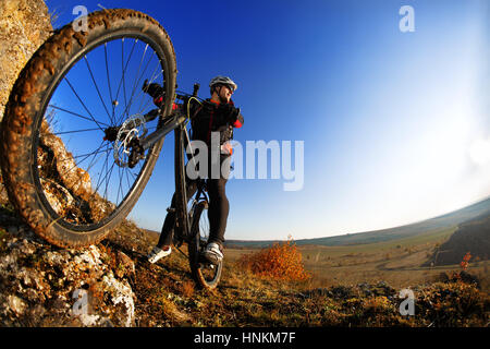 niedrigen Winkel Ansicht des Radfahrers stehend mit Mountain-Bike gegen die helle Sonne und blauer Himmel. Stockfoto