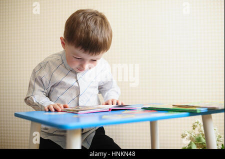 kleiner Junge am Schreibtisch sitzt und liest ein Buch Stockfoto