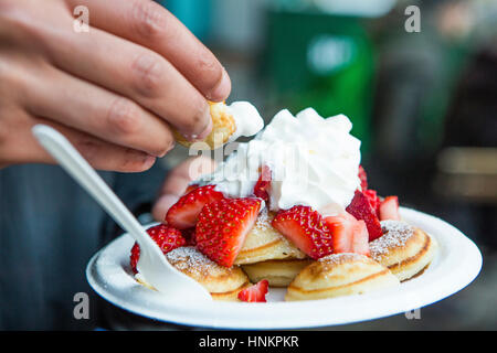 Amerikanische Pfannkuchen mit Erdbeeren und Sahne mit mans hand. Stockfoto