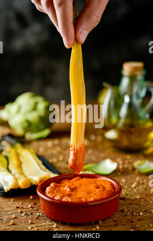 Nahaufnahme eines Mannes Eintauchen einer gerösteten Calcot von Katalonien, Spanien, in Romesco-Sauce, und einige Calcots und eine Menage mit Olivenöl auf typischen süßen Zwiebeln Stockfoto