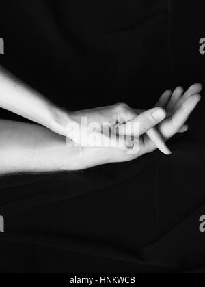 Schwarz / weiß Bild, Hände von Mann und Frau, die Hand in Hand zärtlich auf schwarzem Hintergrund Stockfoto