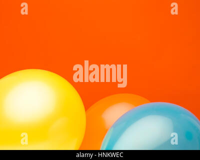dreidimensionale Ballons gelb, Orange und blau vor rotem Hintergrund Stockfoto