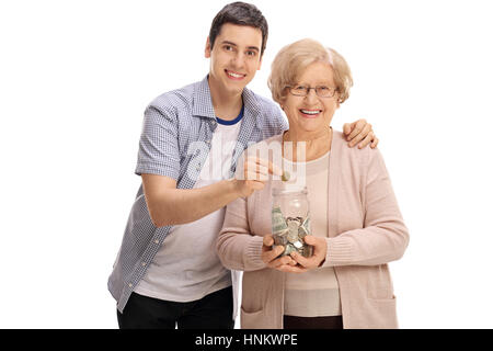 Reife Frau hält ein Geld-Glas mit einem jungen Mann, eine Münze in es isoliert auf weißem Hintergrund Stockfoto