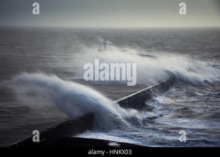 Riesige Wellen über einen Deich in der Nähe von einem Leuchtturm während eines Sturms Stockfoto