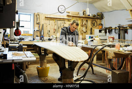 Mann stehend in einem Workshop Schleifen und Gestaltung einer hölzernen Surfbrett. Stockfoto