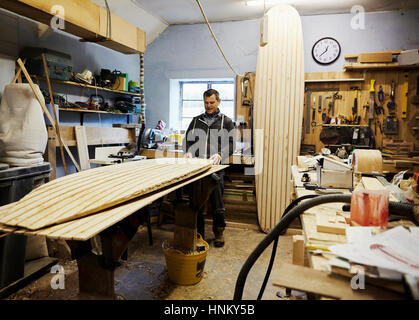 Ein Surfbrett-Workshop, eine lange an Bord beugte aufrecht und ein Brett in der Produktion auf einer Werkbank. Surfbrett-Hersteller bei der Arbeit. Stockfoto