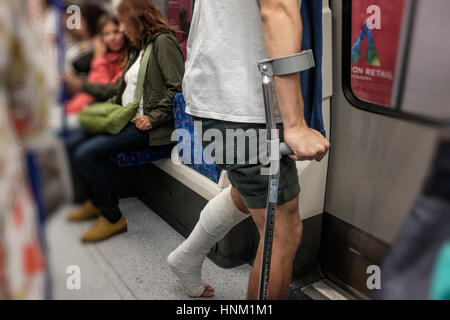 Mann auf Krücken mit Gips auf öffentliche Verkehrsmittel, U-Bahn London, England