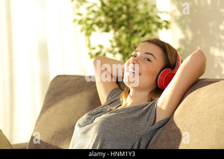 Ein Teenager Musik über Kopfhörer hören und betrachten Sie sitzen auf einer Couch im Wohnzimmer zu Hause mit einem warmen Licht im Hintergrund Stockfoto