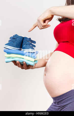 Schwangere Frau, die Kleidung für Baby, Konzept der Familie erweitern und erwartet für Neugeborene Stockfoto