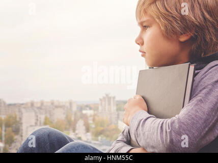 Junge mit Buch sitzen und durch die Fenster schaut nachdenklich träumen Stockfoto