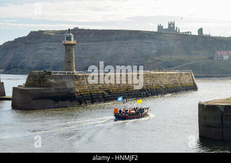 Leuchtturm mit Whitby Abtei und Kirche der Heiligen Maria im Hintergrund. Touristischen Rettungsboot im Vordergrund. Stockfoto