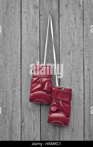 Rote Leder Boxhandschuhe an den Nagel hängt, grau geknackt Holzwand Stockfoto