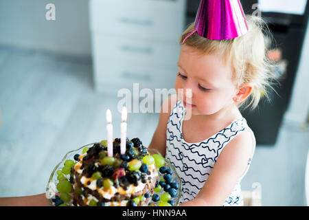 Niedliche kleine Mädchen mit ihrem Obst-Torte mit zwei Kerzen Stockfoto