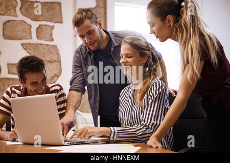 Glückliches Junges Team lacht und zeigt auf dem Laptop sind sie für ihr Business-Meeting im Büro teilen. Stockfoto