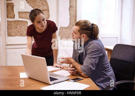 Zwei junge Berufstätige in einem Gespräch mit dem Unternehmer eine Frage mit der linken Hand ihr gestikulieren Stockfoto