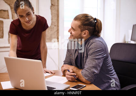 Zwei junge Berufstätige in einem Gespräch mit der Business-Frau zeigt ihm etwas auf dem Bildschirm des Laptops während er an ihr sucht Stockfoto