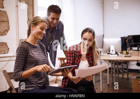 Team von drei jungen Geschäftsleuten suchen sehr glücklich, während eine Dame etwas auf dem Tablett gerichtet ist, die sie hält Stockfoto