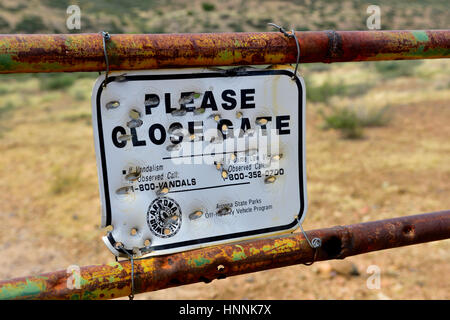 Melden Sie "Bitte enge Tor" voll der Einschusslöcher auf alten rostigen Tor, Ranchland in Landschaft in der Nähe von Dewey Arizona, USA Stockfoto