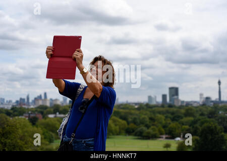 Eine Frau nimmt ein Selfie Foto auf einem Tablett in Primrose Hill, London. Stockfoto