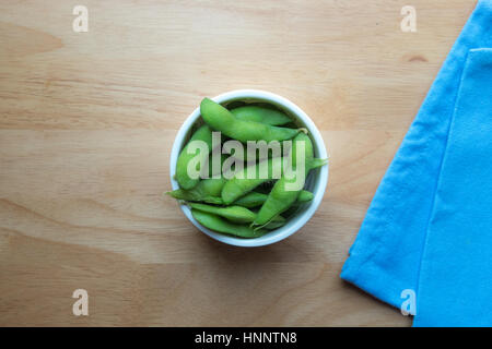 Eine Draufsicht des grüne Sojabohnen in weiße Tasse mit blauem Tuch am Holztisch Hintergrund. Stockfoto