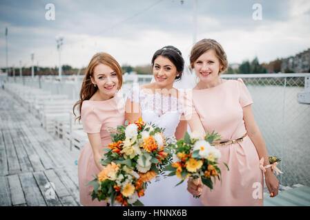 Braut mit Brautjungfern stellte auf der Pier-Liegeplatz am bewölkten Hochzeitstag. Stockfoto