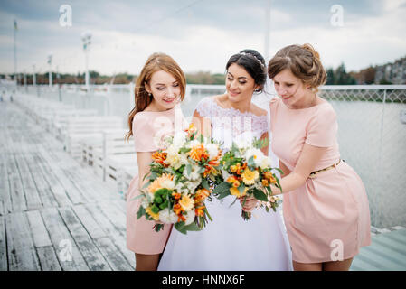 Braut mit Brautjungfern stellte auf der Pier-Liegeplatz am bewölkten Hochzeitstag. Stockfoto