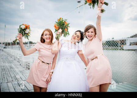 Braut mit Brautjungfern stellte auf der Pier-Liegeplatz am bewölkten Hochzeitstag. Stockfoto