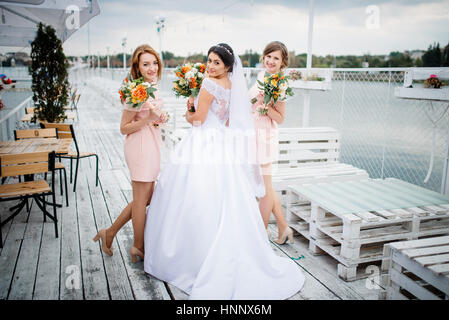 Braut mit Brautjungfern stellte auf der Pier-Liegeplatz am bewölkten Hochzeitstag. Stockfoto