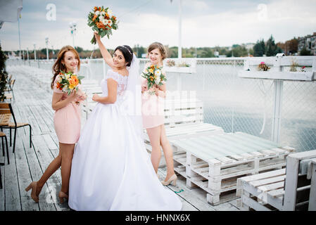 Braut mit Brautjungfern stellte auf der Pier-Liegeplatz am bewölkten Hochzeitstag. Stockfoto