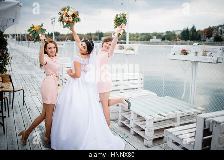 Braut mit Brautjungfern stellte auf der Pier-Liegeplatz am bewölkten Hochzeitstag. Stockfoto