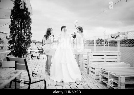 Braut mit Brautjungfern stellte auf der Pier-Liegeplatz am bewölkten Hochzeitstag. Schwarz / weiß Foto. Stockfoto