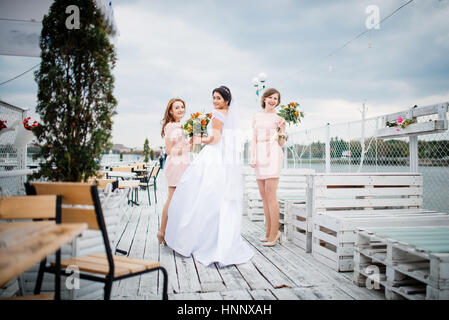 Braut mit Brautjungfern stellte auf der Pier-Liegeplatz am bewölkten Hochzeitstag. Stockfoto