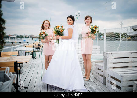 Braut mit Brautjungfern stellte auf der Pier-Liegeplatz am bewölkten Hochzeitstag. Stockfoto