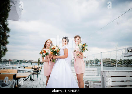 Braut mit Brautjungfern stellte auf der Pier-Liegeplatz am bewölkten Hochzeitstag. Stockfoto