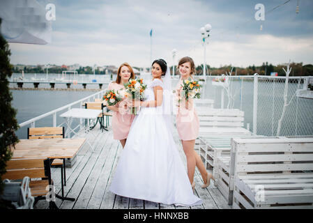 Braut mit Brautjungfern stellte auf der Pier-Liegeplatz am bewölkten Hochzeitstag. Stockfoto