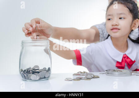 Kleine Asiatin in Thai Studenten Uniform, Münze, Glas mit Mutter Hand zur Einsparung von Geld Fokus auf Händen geringe Schärfentiefe Stockfoto