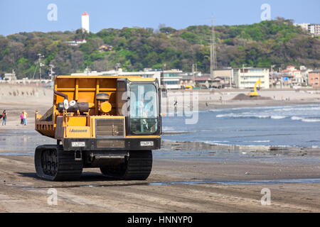 KAMAKURA, JAPAN - ca. April 2013: Crawler Transporter voller Sand fährt am Sandstrand auf der Küste des Pazifischen Ozeans. Kommunale Strand Verbesserungsarbeiten Stockfoto