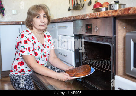 Senior kaukasischen Frau mit einem Kuchen in Händen der Einbau-Backofen in der Küche saß Stockfoto