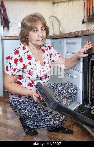 Reife Frau kaukasischen saß der Einbau-Backofen mit offener Tür. Heimischen Küche Stockfoto