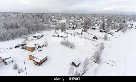 Ländliche Häuser und Scheunen sind auf Winter Seeufer. Russische abgelegenes Dorf in immergrünen Wäldern. Luftaufnahme. Russland Stockfoto