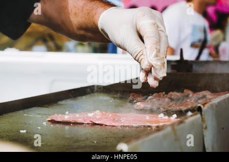 Nahaufnahme der Hand eines Küchenchefs, der Handschuhe trägt und Salz hinzufügt A zu einem Stück auf dem Grill treffen Stockfoto