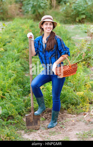 Herbst Ernte Konzept. Glücklich lächelnd kaukasischen weibliche Landwirt oder Gärtner mit Spaten und Korb mit geernteten Gemüse. Frau arbeitet im g Stockfoto