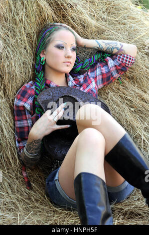 junge tätowierte stilvolle Frau mit Dreadlocks in Cowgirl Stil, entspannend auf Heuhaufen Stockfoto