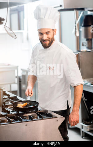 Hübscher Chef-Koch in Uniform, Kochen auf dem Gasherd in der Küche Stockfoto