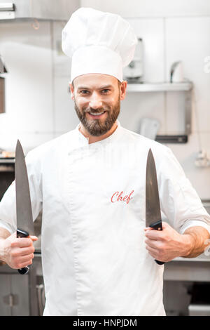 Porträt von Chef-Koch in Uniform mit Messern in der Restaurantküche Stockfoto