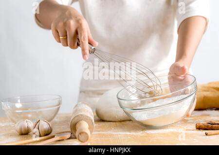 Fehlschüsse Händen Frau mit Edelstahl Schneebesen und Bäckerei Teig Mehl in Glasschale, geringe Schärfentiefe, Fokus auf Schüssel hautnah Stockfoto