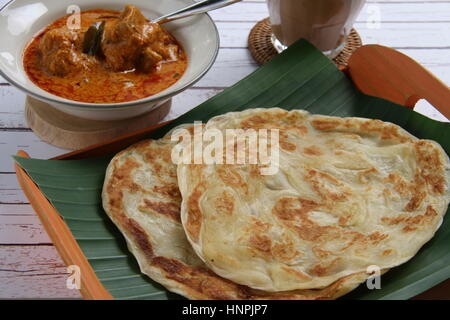 Roti Prata. Fladenbrot mit indischen beeinflusst. Vergoldete auf einem Banane Blatt-gesäumten Bambus-Tablett mit Hühnchen-Curry, die separat auf eine Keramikschale serviert. Stockfoto