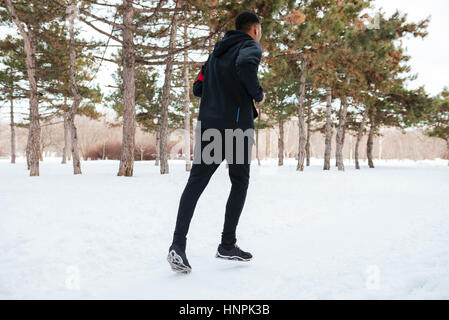 Rückansicht eines jungen Mannes mit Schnee bedeckte Winter unterwegs im Wald Stockfoto