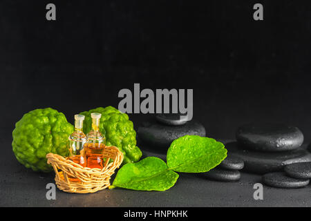 aromatische Konzept der Bergamotte, Blatt, Duft-Öl und Zen Basaltsteinen mit Wassertropfen auf schwarzem Hintergrund, Nahaufnahme Stockfoto